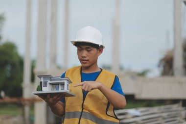 Genç yakışıklı Asyalı inşaat mühendisi elinde tabletle ileriye bakıyor ve düşünüyor, inşaat geçmişini planlıyor. Evrim inşa kavramı.