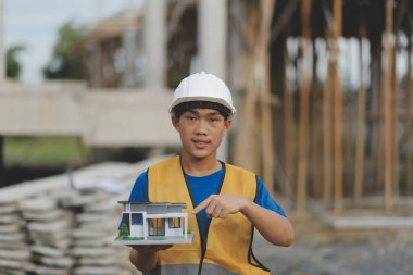 Genç yakışıklı Asyalı inşaat mühendisi elinde tabletle ileriye bakıyor ve düşünüyor, inşaat geçmişini planlıyor. Evrim inşa kavramı.