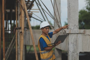 Genç yakışıklı Asyalı inşaat mühendisi elinde tabletle ileriye bakıyor ve düşünüyor, inşaat geçmişini planlıyor. Evrim inşa kavramı.