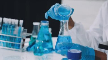 Laboratuvar bilim adamı elinde mavi sıvıyla matarayı tutuyor.