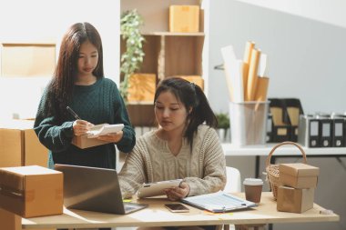 Başlangıçta küçük işletme KOBİ 'si, akıllı telefon veya tablet kullanan girişimci Afrikalı kadın paket ürün kutusu hazırlamak için çevrimiçi alışveriş siparişini alır ve kontrol eder.