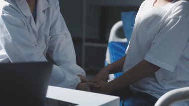 Beyaz önlüklü doktor ve hasta elleri hastane odasında el ele tutuşuyor..