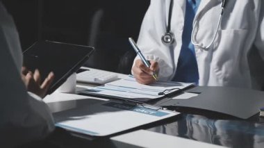 Doktor elinde tıbbi belgeler ve hasta ile tablet tutuyor.