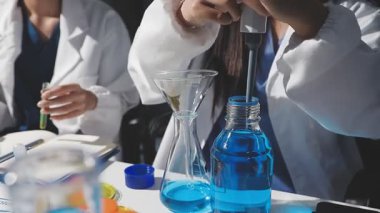 Mavi üniformalı genç bir bilim adamının elinde elinde sıvı olan bir tüp tutarken. Bilim, teknoloji, araştırma, öğrenim ve geliştirme