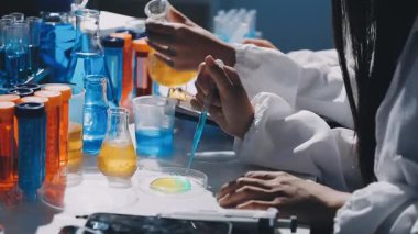 Koruyucu üniformalı genç bir bilim adamı elinde matarayla laboratuvar malzemeleriyle deney yapıyor.