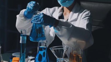 Üniformalı kadın laboratuvar çalışanının elinde test tüpü ve sıvı şişeyle yakın görüntüsü.