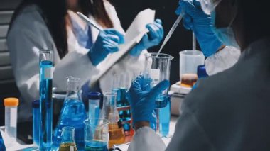 Mavi takım elbiseli bir laboratuvar asistanı ve eldivenler bir şişe dolusu sıvı tutuyor..