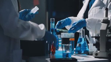 Mavi üniformalı laboratuvar asistanı ve ellerinde test tüpü tutan eldivenler.