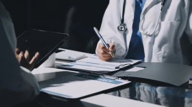 Doktor elinde dijital tablet tutuyor ve hastane ofisindeki masada notlar yazıyor. Sağlık ve teknoloji kavramı