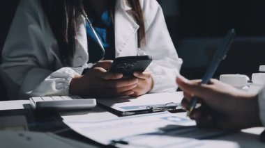 Beyaz üniformalı doktor, hastane masasında otururken elinde haplar ve haplar tutuyor.