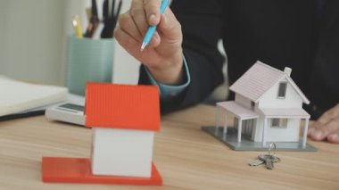 Adam el ele tutuşup masasında ev modeli olan bir yığın kağıt tutuyor.