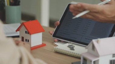 Emlakçı elinde tablet ve ev modelinin anahtarını gösteriyor..