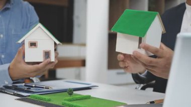 Emlakçı ev modelini tutuyor ve tabela gösteriyor.