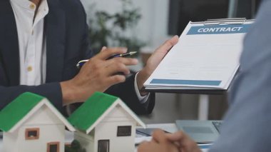 Emlakçı ev modeli ile el sıkışıyor, kontrat imzalıyor.