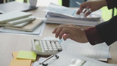 İş adamları ofiste hesap makinesi üzerinde çalışıyor ve notlar yazıyor.