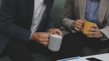 Genç Asyalı bir adam bir fincan kahve tutuyor ve tablet bilgisayar kullanıyor.