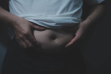 Asyalı şişman bir adam aynanın önünde vücuduna bakıyor. Aşırı göbek yağı, sağlıksız yaşam tarzı, diyet konsepti.