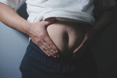 Asyalı şişman bir adam aynanın önünde vücuduna bakıyor. Aşırı göbek yağı, sağlıksız yaşam tarzı, diyet konsepti.