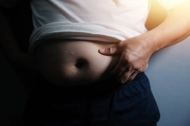 Asyalı şişman bir adam aynanın önünde vücuduna bakıyor. Aşırı göbek yağı, sağlıksız yaşam tarzı, diyet konsepti.