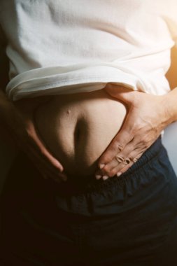 Asyalı şişman bir adam aynanın önünde vücuduna bakıyor. Aşırı göbek yağı, sağlıksız yaşam tarzı, diyet konsepti.