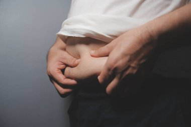 Asyalı şişman bir adam aynanın önünde vücuduna bakıyor. Aşırı göbek yağı, sağlıksız yaşam tarzı, diyet konsepti.