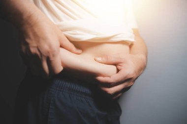 Asyalı şişman bir adam aynanın önünde vücuduna bakıyor. Aşırı göbek yağı, sağlıksız yaşam tarzı, diyet konsepti.