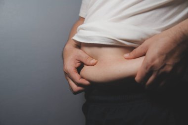 Asyalı şişman bir adam aynanın önünde vücuduna bakıyor. Aşırı göbek yağı, sağlıksız yaşam tarzı, diyet konsepti.