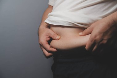 Asyalı şişman bir adam aynanın önünde vücuduna bakıyor. Aşırı göbek yağı, sağlıksız yaşam tarzı, diyet konsepti.