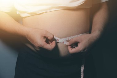 Asyalı şişman bir adam aynanın önünde vücuduna bakıyor. Aşırı göbek yağı, sağlıksız yaşam tarzı, diyet konsepti.