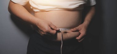 Asyalı şişman bir adam aynanın önünde vücuduna bakıyor. Aşırı göbek yağı, sağlıksız yaşam tarzı, diyet konsepti.