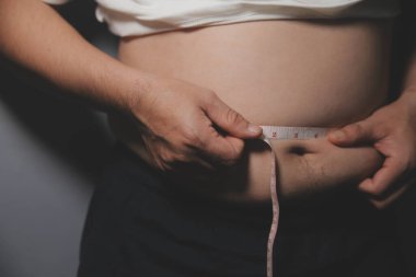 Asyalı şişman bir adam aynanın önünde vücuduna bakıyor. Aşırı göbek yağı, sağlıksız yaşam tarzı, diyet konsepti.