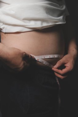 Asyalı şişman bir adam aynanın önünde vücuduna bakıyor. Aşırı göbek yağı, sağlıksız yaşam tarzı, diyet konsepti.