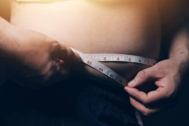 Asyalı şişman bir adam aynanın önünde vücuduna bakıyor. Aşırı göbek yağı, sağlıksız yaşam tarzı, diyet konsepti.