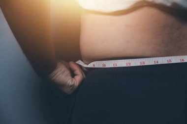 Asyalı şişman bir adam aynanın önünde vücuduna bakıyor. Aşırı göbek yağı, sağlıksız yaşam tarzı, diyet konsepti.