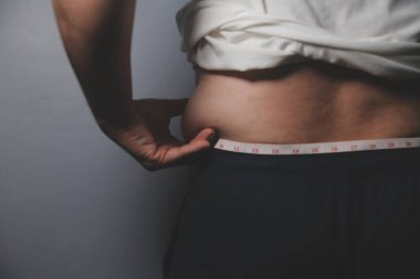 Asyalı şişman bir adam aynanın önünde vücuduna bakıyor. Aşırı göbek yağı, sağlıksız yaşam tarzı, diyet konsepti.