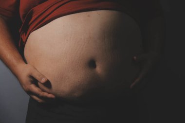 Asyalı şişman bir adam aynanın önünde vücuduna bakıyor. Aşırı göbek yağı, sağlıksız yaşam tarzı, diyet konsepti.