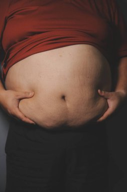 Asyalı şişman bir adam aynanın önünde vücuduna bakıyor. Aşırı göbek yağı, sağlıksız yaşam tarzı, diyet konsepti.