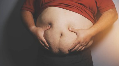 Asyalı şişman bir adam aynanın önünde vücuduna bakıyor. Aşırı göbek yağı, sağlıksız yaşam tarzı, diyet konsepti.