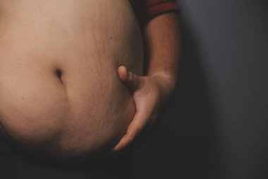 Asyalı şişman bir adam aynanın önünde vücuduna bakıyor. Aşırı göbek yağı, sağlıksız yaşam tarzı, diyet konsepti.