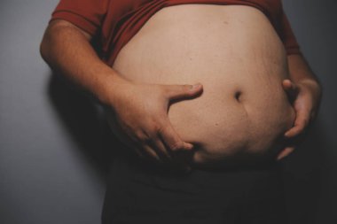 Asyalı şişman bir adam aynanın önünde vücuduna bakıyor. Aşırı göbek yağı, sağlıksız yaşam tarzı, diyet konsepti.