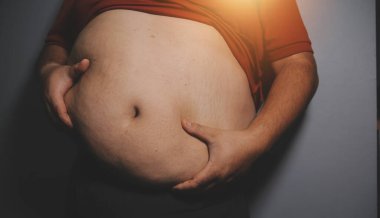 Asyalı şişman bir adam aynanın önünde vücuduna bakıyor. Aşırı göbek yağı, sağlıksız yaşam tarzı, diyet konsepti.