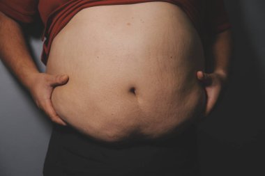 Asyalı şişman bir adam aynanın önünde vücuduna bakıyor. Aşırı göbek yağı, sağlıksız yaşam tarzı, diyet konsepti.