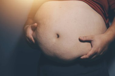 Asyalı şişman bir adam aynanın önünde vücuduna bakıyor. Aşırı göbek yağı, sağlıksız yaşam tarzı, diyet konsepti.