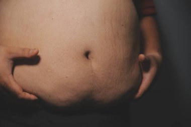 Asyalı şişman bir adam aynanın önünde vücuduna bakıyor. Aşırı göbek yağı, sağlıksız yaşam tarzı, diyet konsepti.