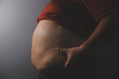 Asyalı şişman bir adam aynanın önünde vücuduna bakıyor. Aşırı göbek yağı, sağlıksız yaşam tarzı, diyet konsepti.