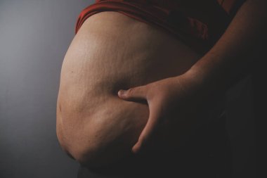 Asyalı şişman bir adam aynanın önünde vücuduna bakıyor. Aşırı göbek yağı, sağlıksız yaşam tarzı, diyet konsepti.