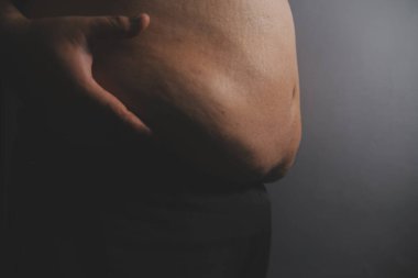 Asyalı şişman bir adam aynanın önünde vücuduna bakıyor. Aşırı göbek yağı, sağlıksız yaşam tarzı, diyet konsepti.