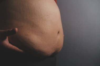 Asyalı şişman bir adam aynanın önünde vücuduna bakıyor. Aşırı göbek yağı, sağlıksız yaşam tarzı, diyet konsepti.