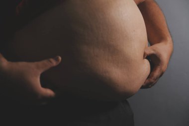 Asyalı şişman bir adam aynanın önünde vücuduna bakıyor. Aşırı göbek yağı, sağlıksız yaşam tarzı, diyet konsepti.