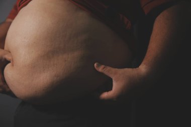 Asyalı şişman bir adam aynanın önünde vücuduna bakıyor. Aşırı göbek yağı, sağlıksız yaşam tarzı, diyet konsepti.